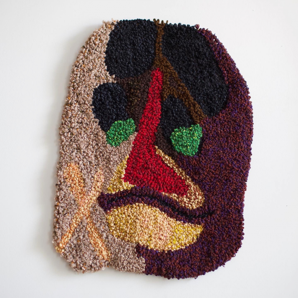 Medium sized punch needle work made of yarn depicting an abstract face.