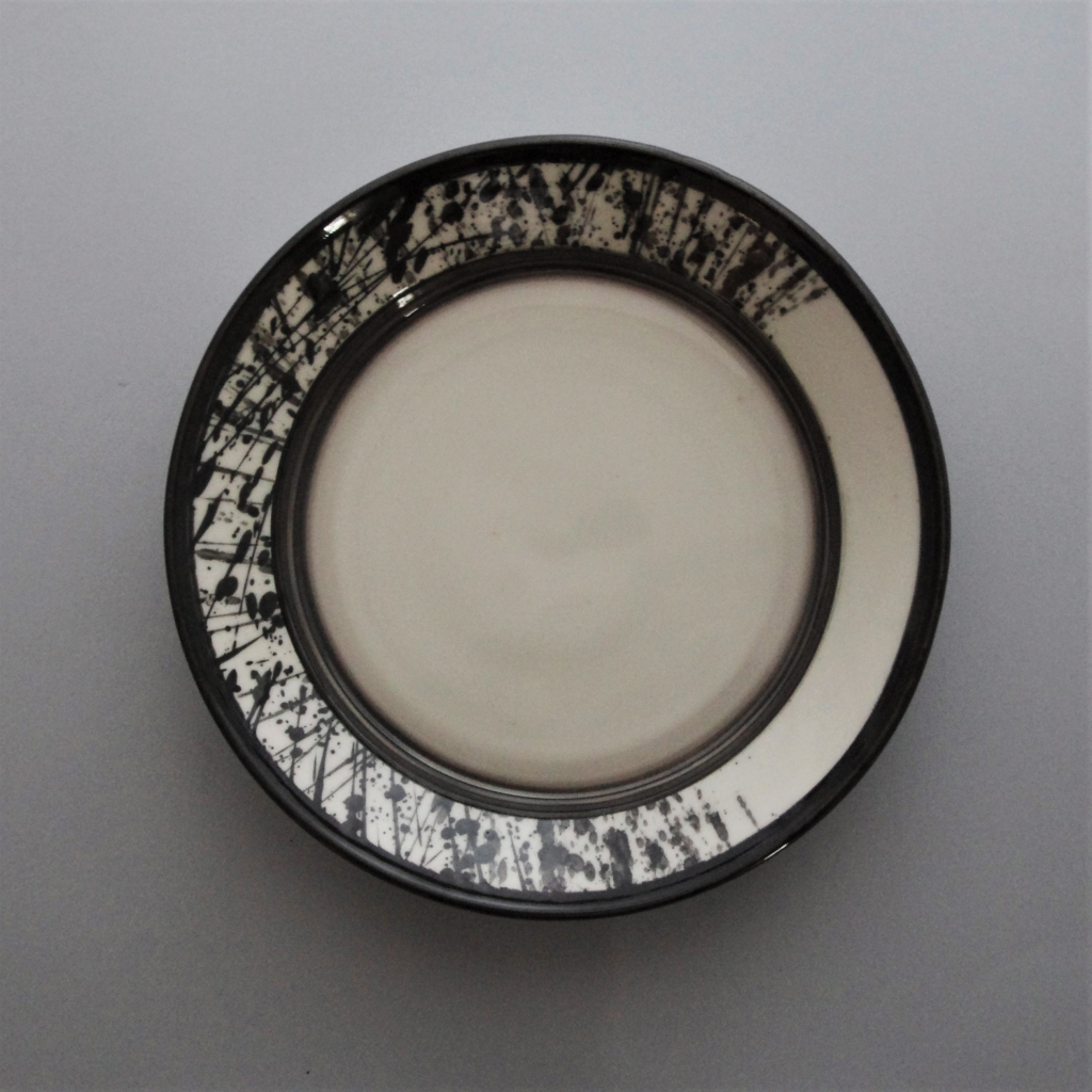 Porcelain plate with black clay splattered in abstract pattern, finished with a clear glaze.