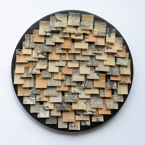 Round panel with black encaustic background and collage of old book pages in small squares attached with beeswax