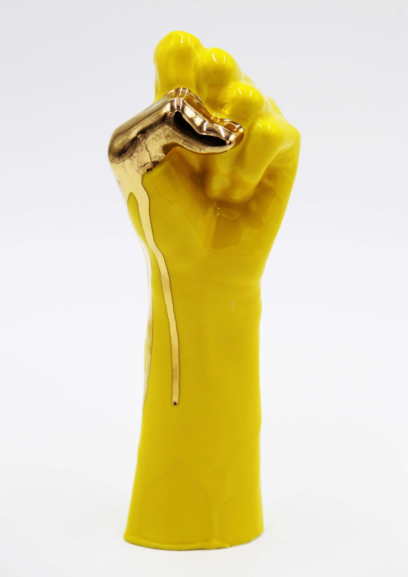 A yellow ceramic hand, wrist and half of a forearm featuring the ASL “S” handshape.