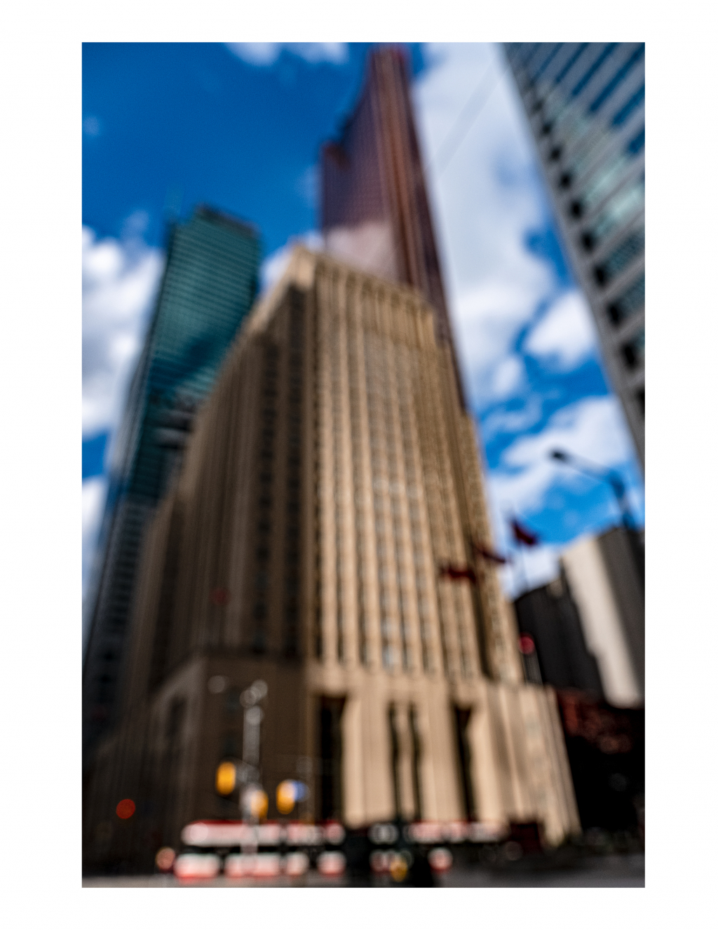 A blurred photo of multiple skyscrapers. A street car passes by at the base of the photo